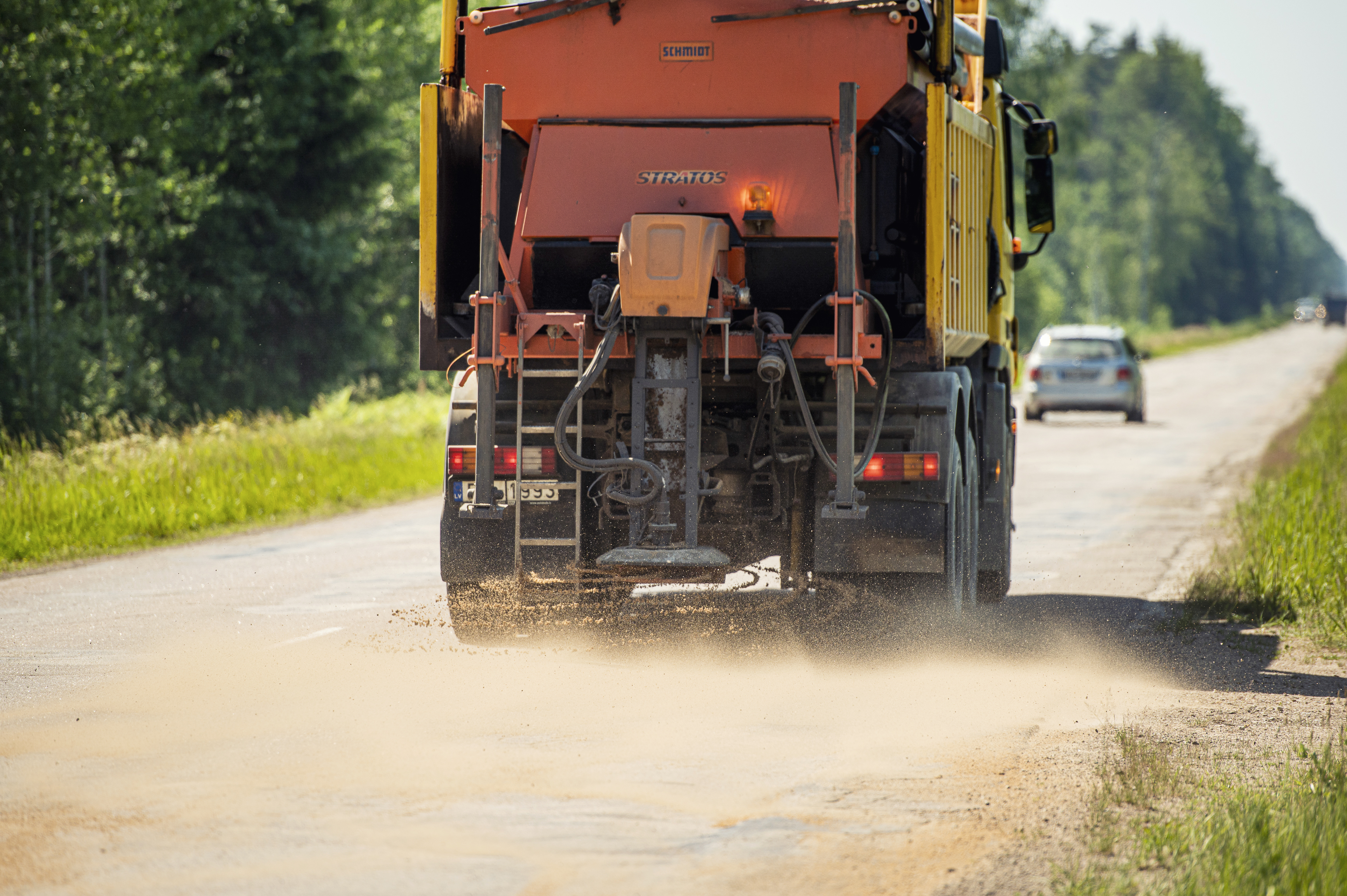 Kravas automašīna kaisa ar smilti autoceļu, uz kura ir izsvīdumi